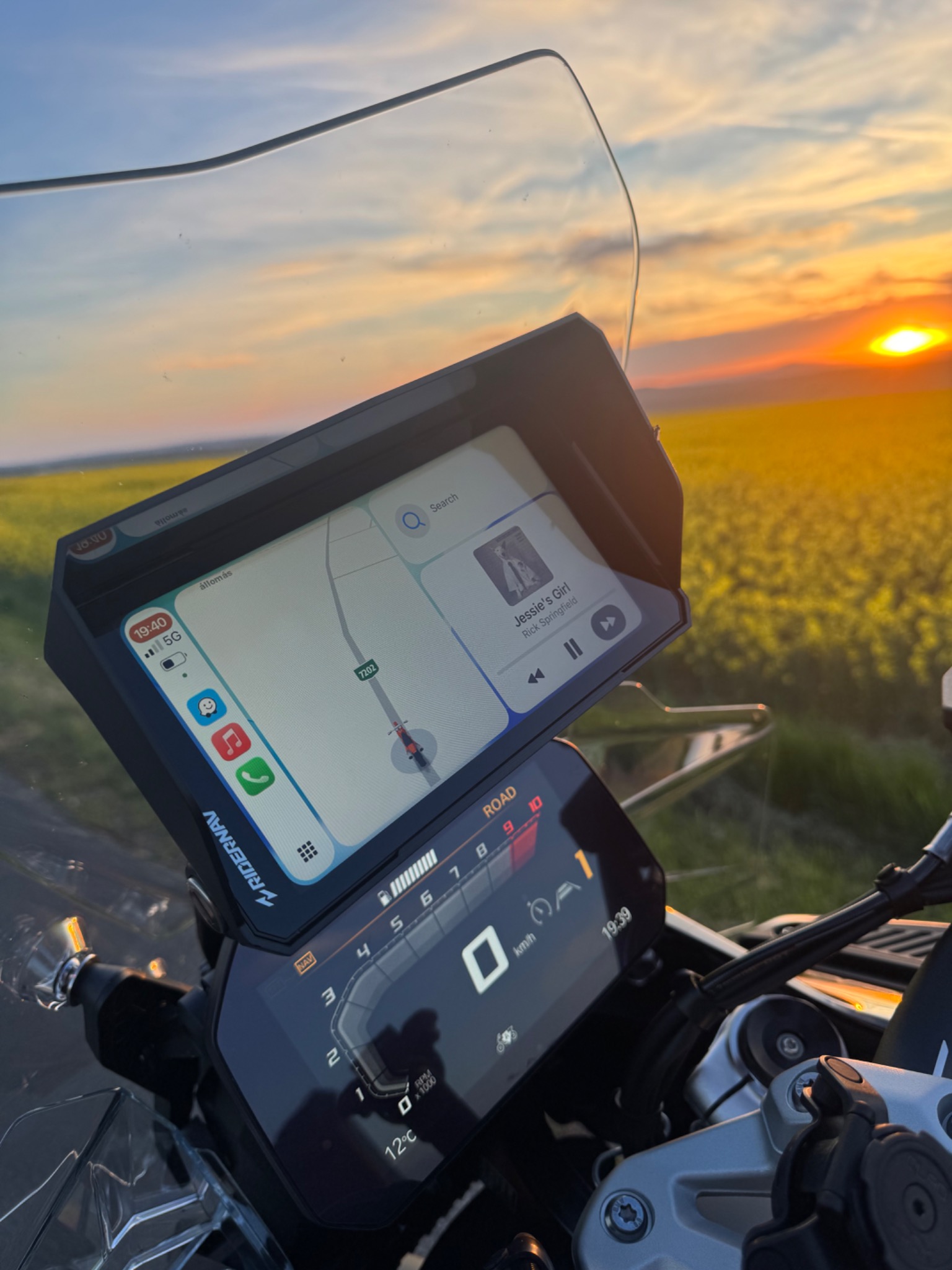 RiderNav R7M showing navigation and music beside a field at sunset